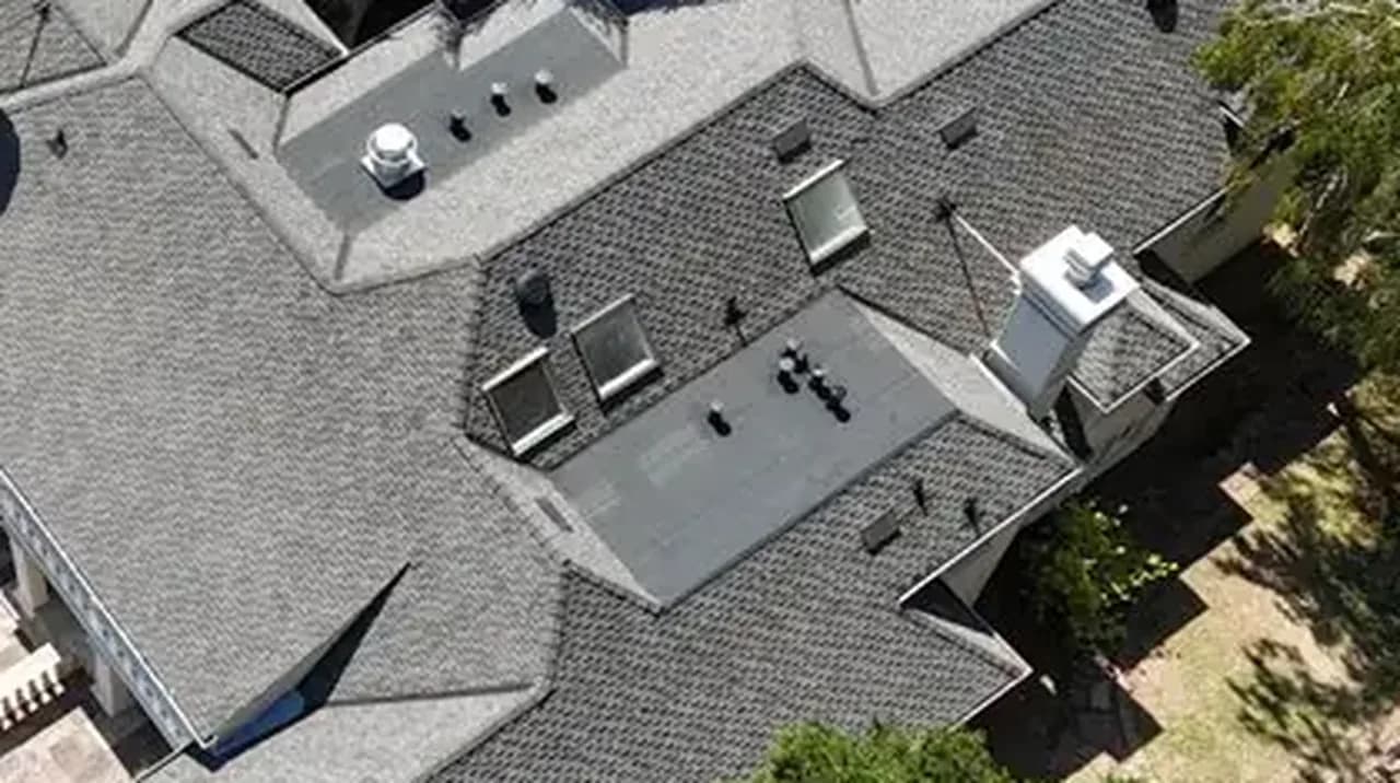 New gray architectural shingle roof seen from above, with ridges, chimneys and skylights